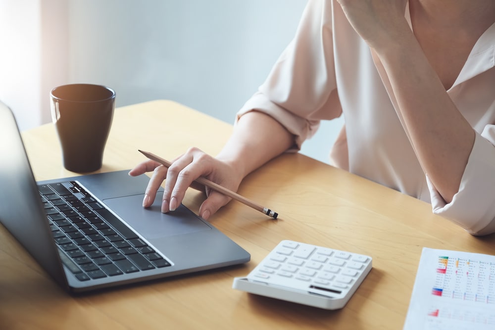 Professionnelle analysant des graphiques financiers avec un ordinateur portable, une calculatrice et un crayon au bureau.