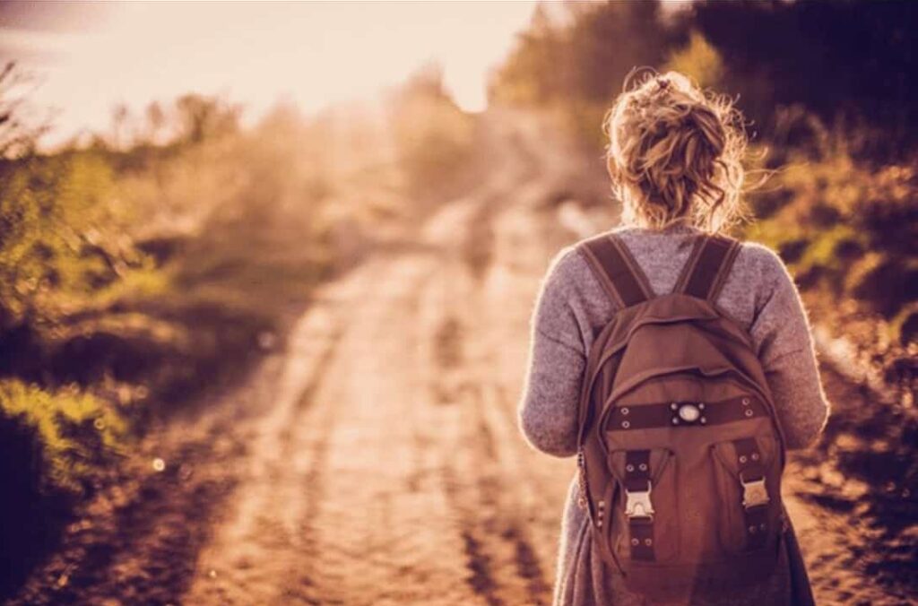 Randonnée au coucher du soleil : femme avec sac à dos Femme avec sac à dos marchant sur un chemin de terre au coucher du soleil dans la nature sauvage.